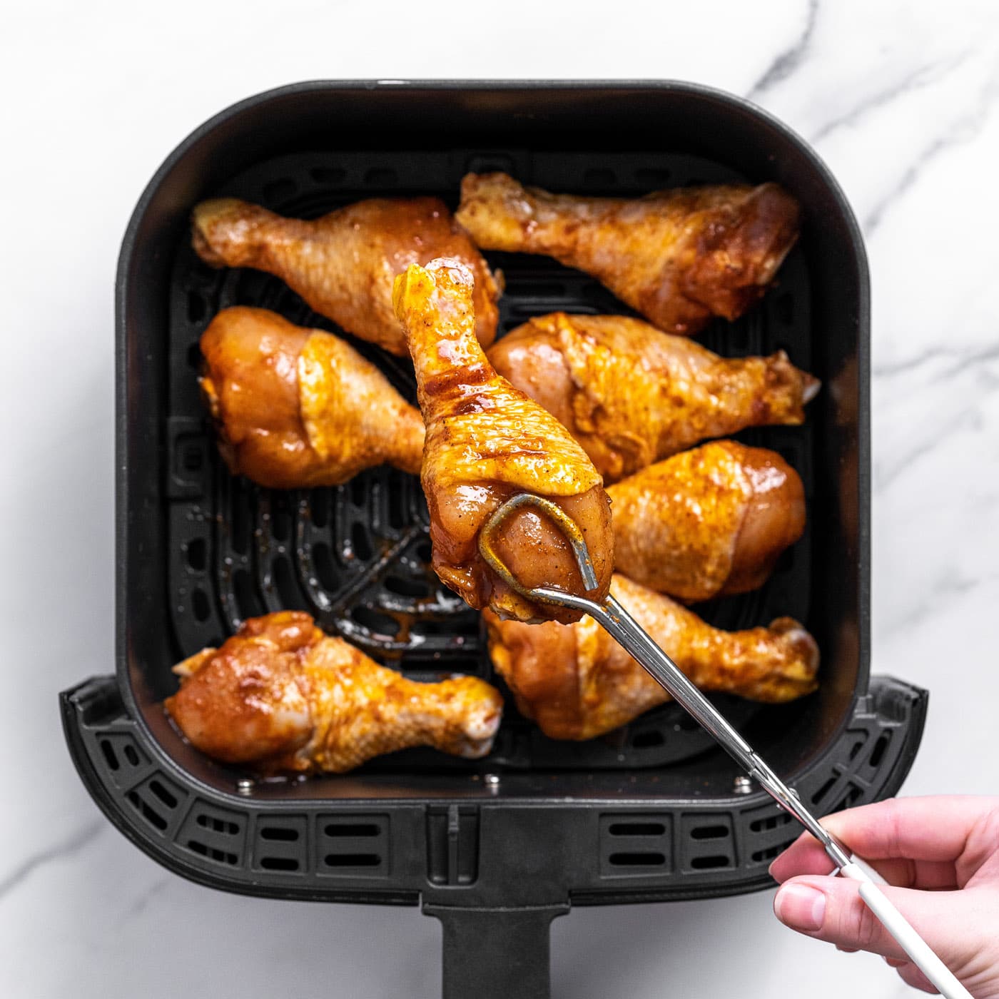 tongs placing chicken leg into air fryer