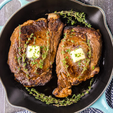 Two Cast Iron Ribeyes in a cast iron pan with butter pats on top