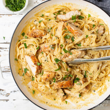Chicken Alfredo in a serving dish with tongs