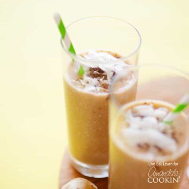 Two tall clear glasses filled with a cozy coconut smoothie and served with a green and white striped straw.