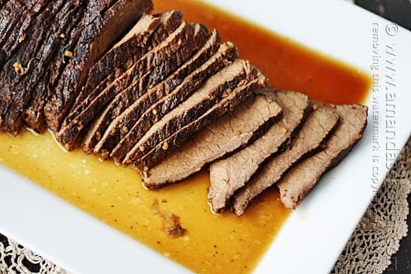 A close up overhead of sliced slow cooker roast with brandy sauce on a white platter.