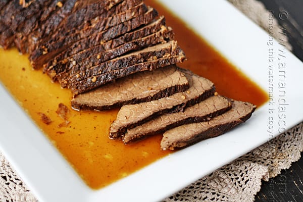 A close up of sliced slow cooker roast with brandy sauce on a white platter.