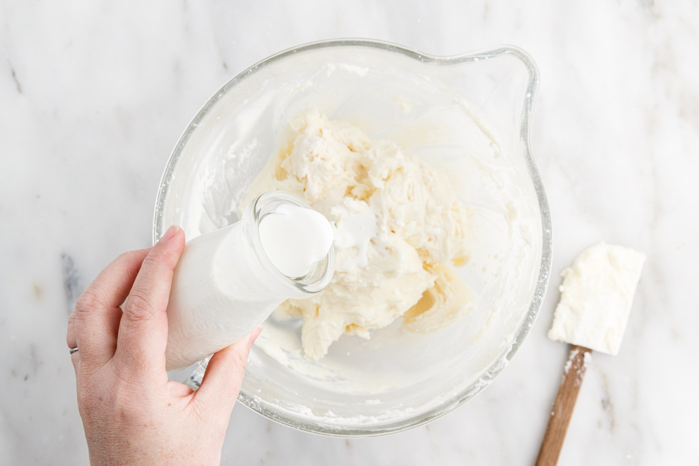 adding cream to frosting in a bowl