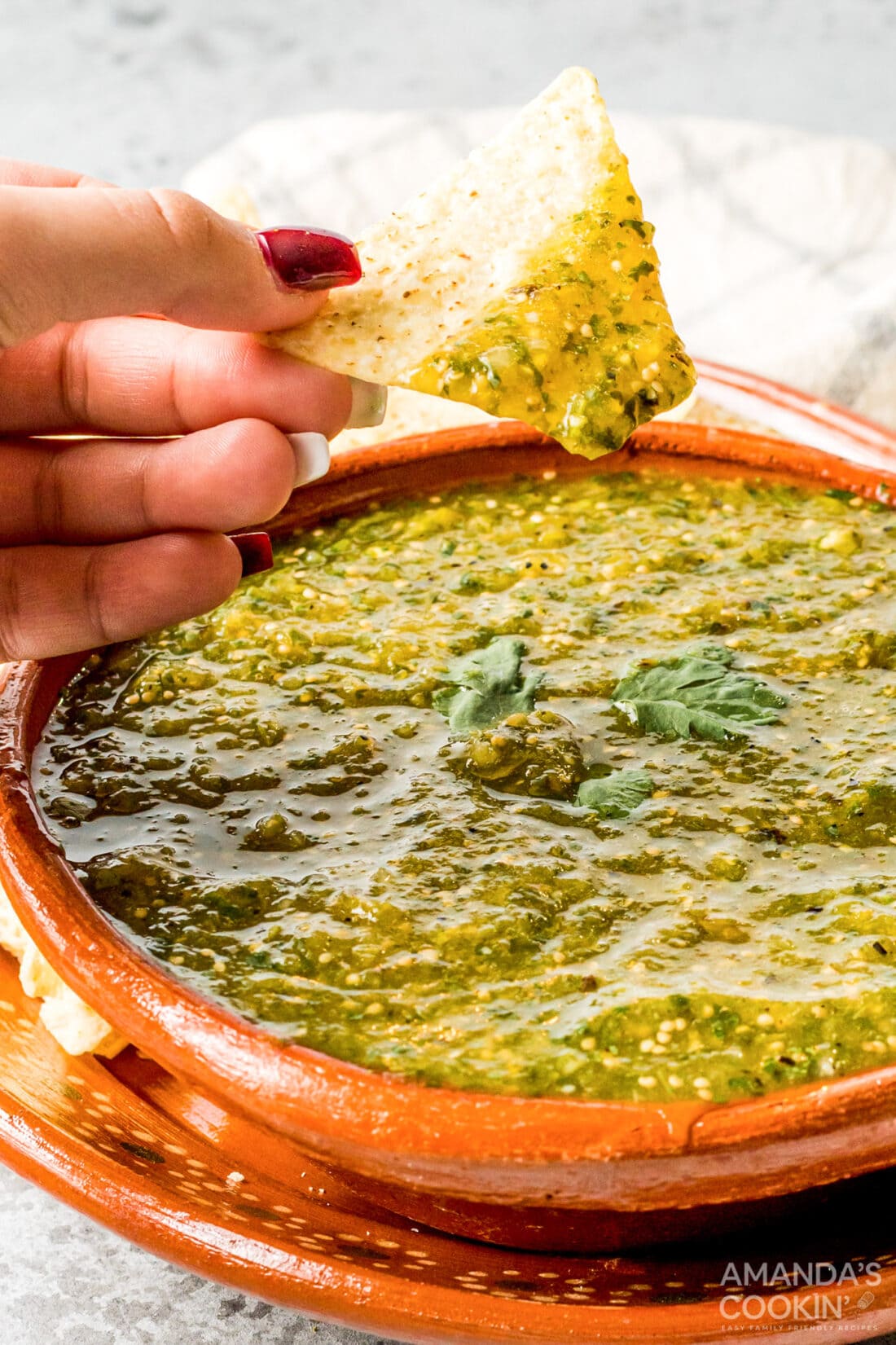 woman's hand scooping green salsa with a tortilla chip
