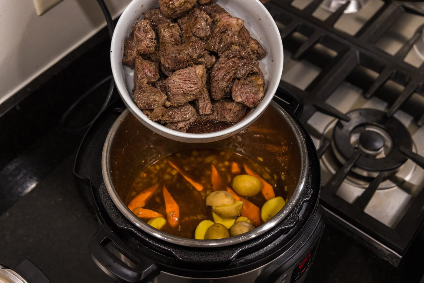 adding browned beef to instant pot with vegetables