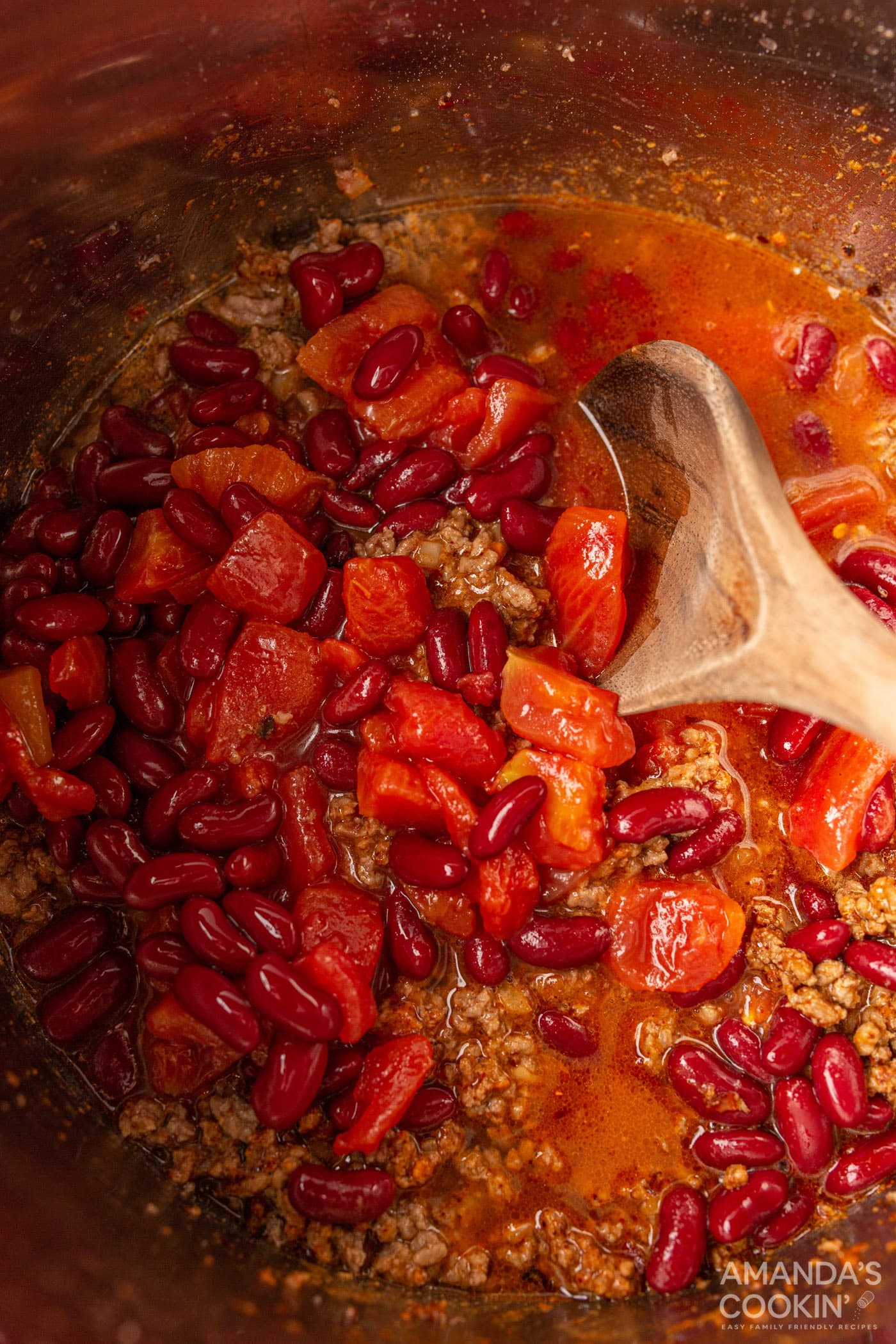 wooden spoon stirring tomatoes into chili