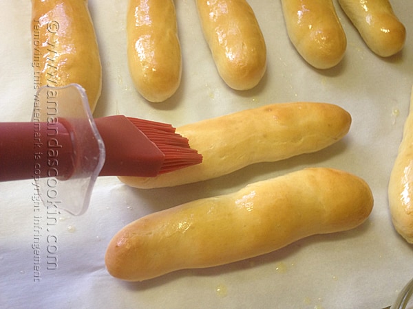 A close up photo of melted butter being brushed onto baked breadsticks.