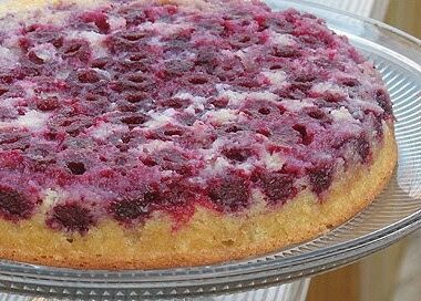 A close up photo of a raspberry upside down cake on a clear cake stand.