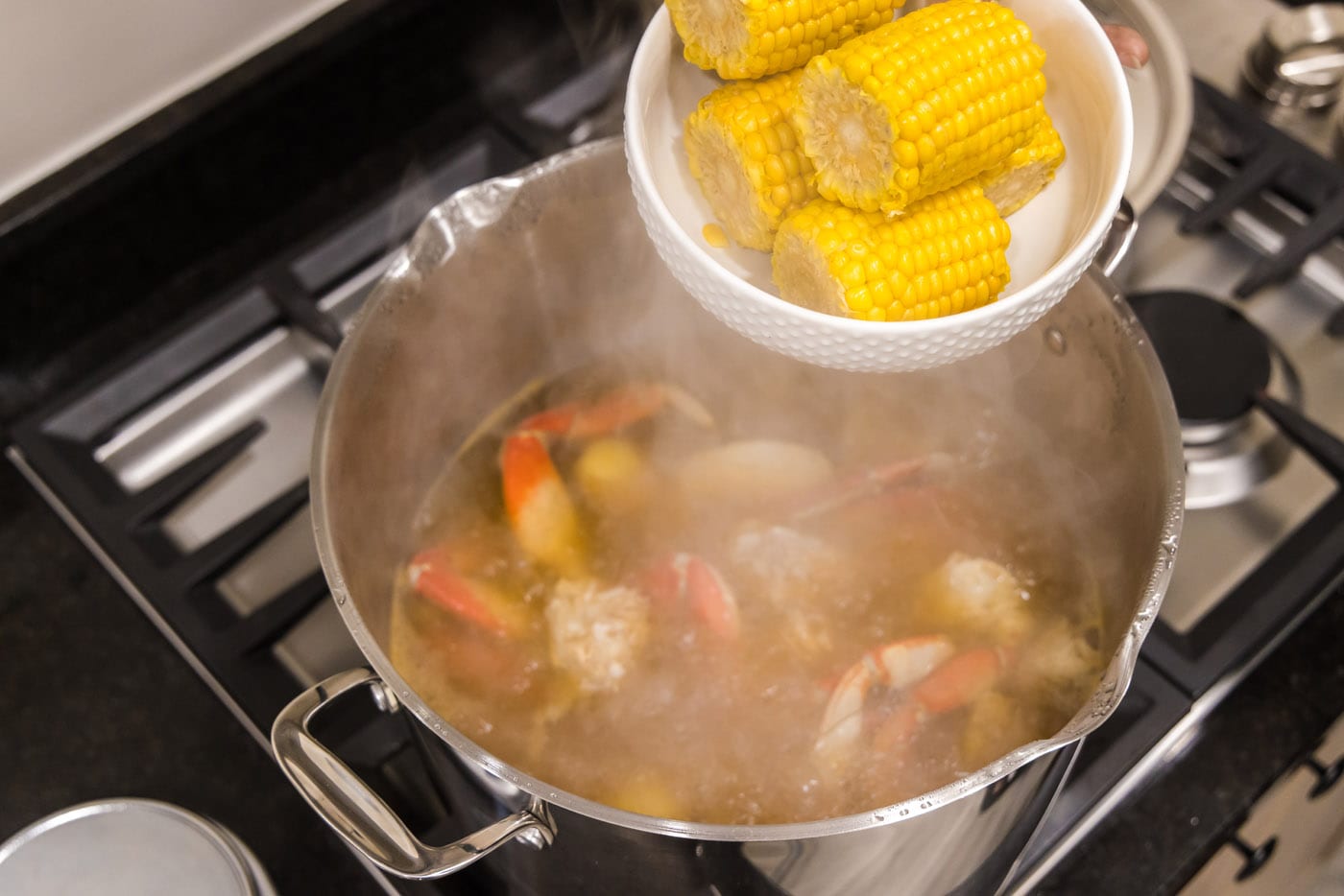 adding corn to pot of water with crab legs
