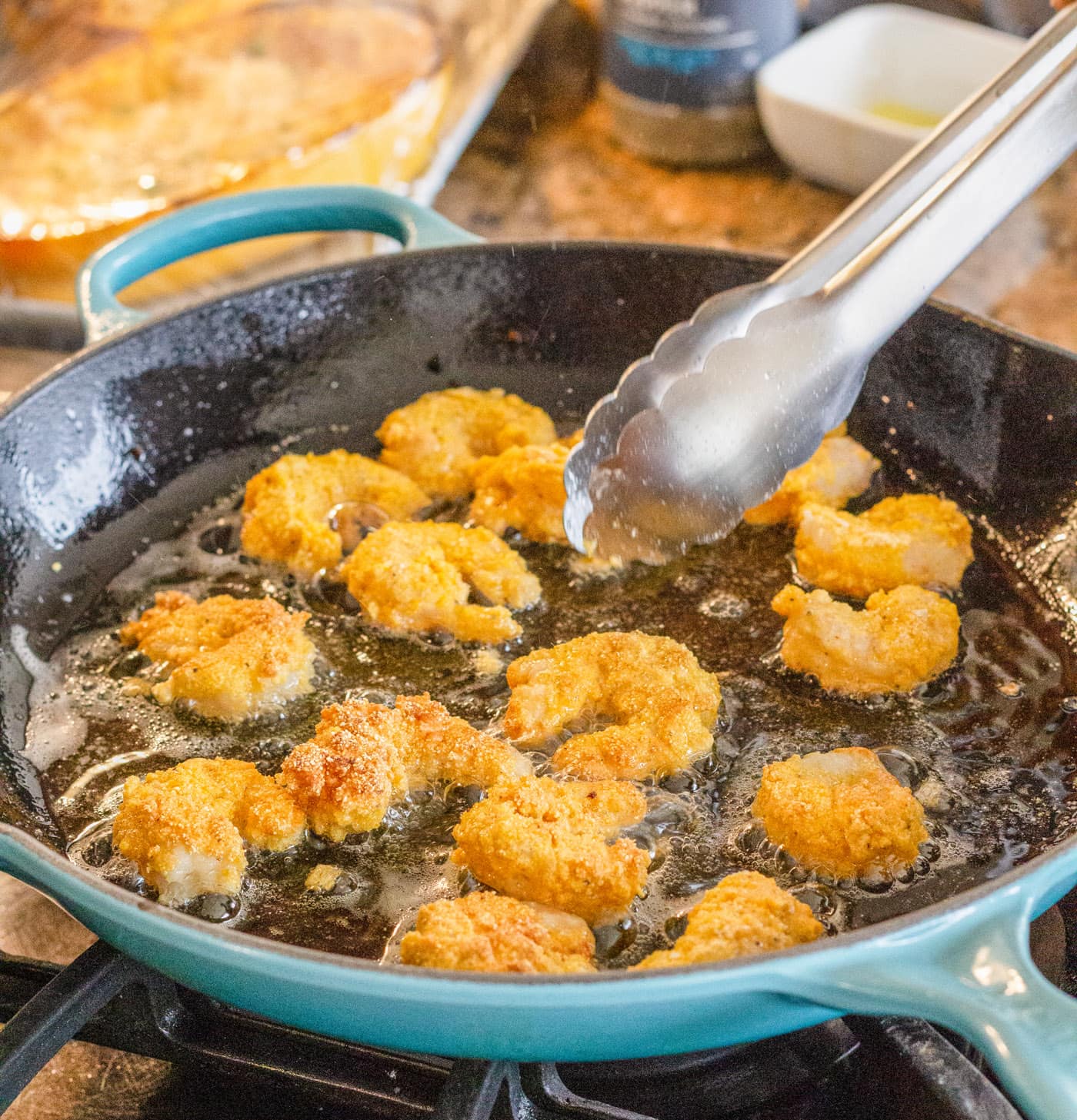 tongs flipping fried shrimp in a skillet